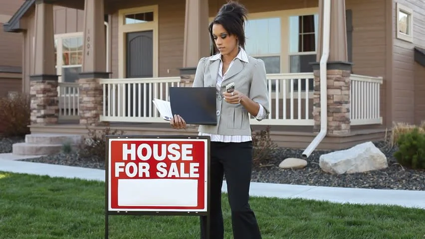 woman standing behind a for sale house in front of a house
