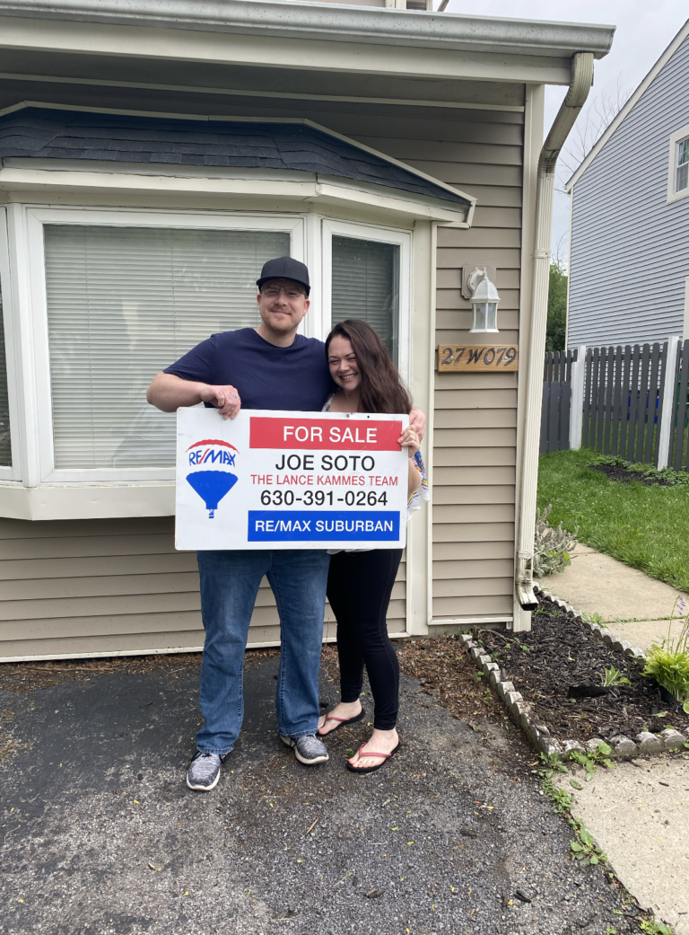 a couple holding a signage for sale in local realtor at re/max